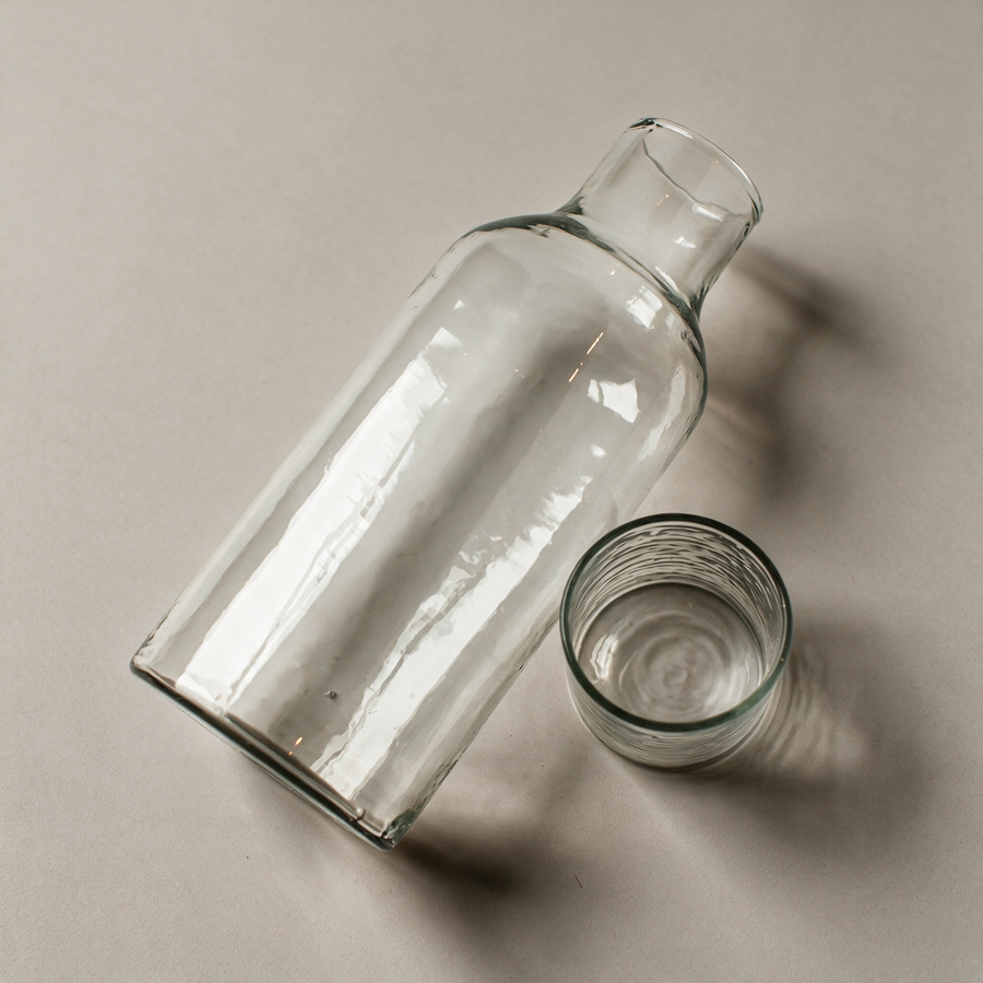 Hand-hammered glass carafe on a warm grey studio background