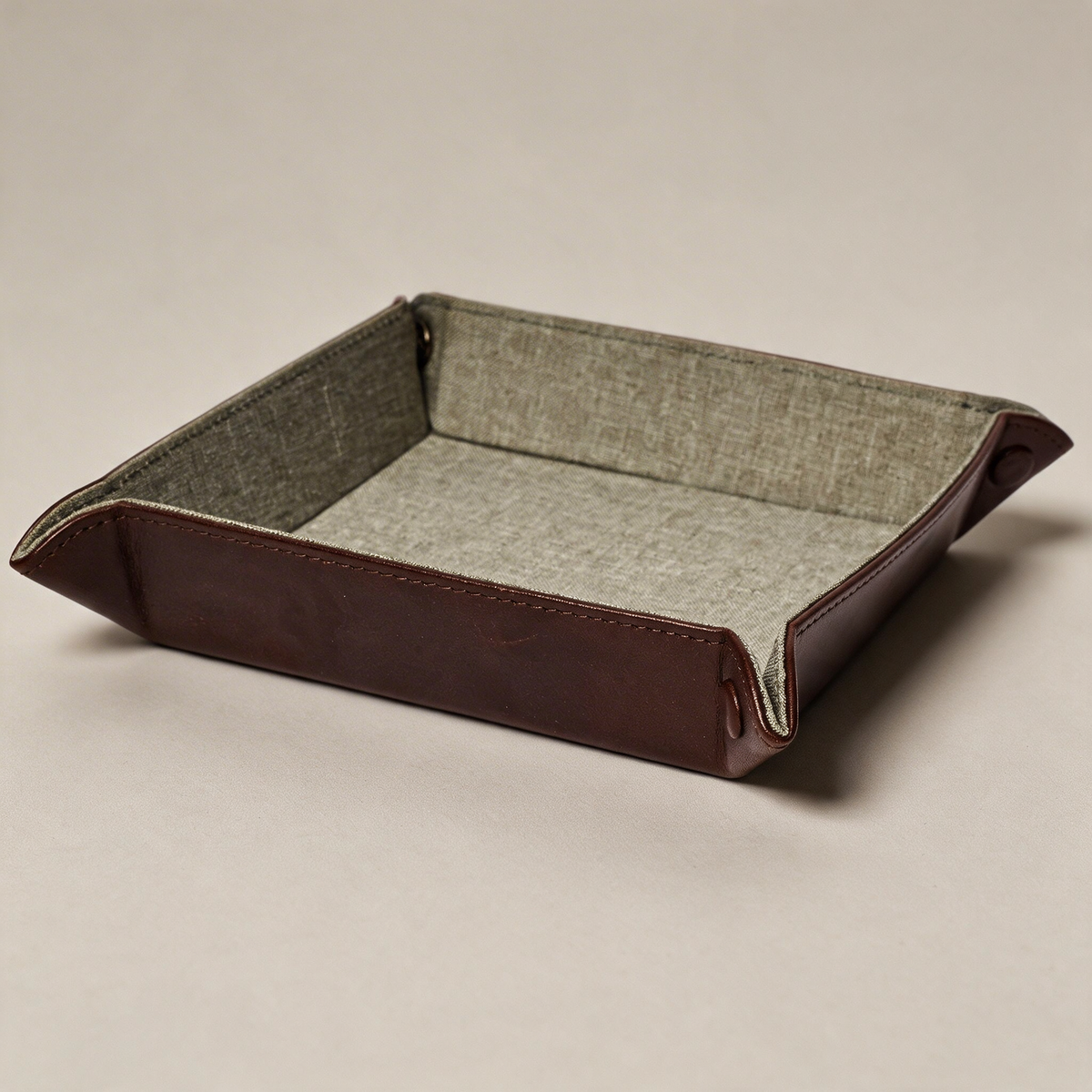 Folding leather valet tray on a warm grey studio background