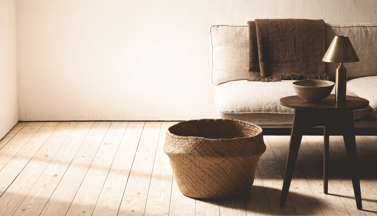 Lived-in room corner with linen sofa, handwoven throw, floor basket and brass lamp