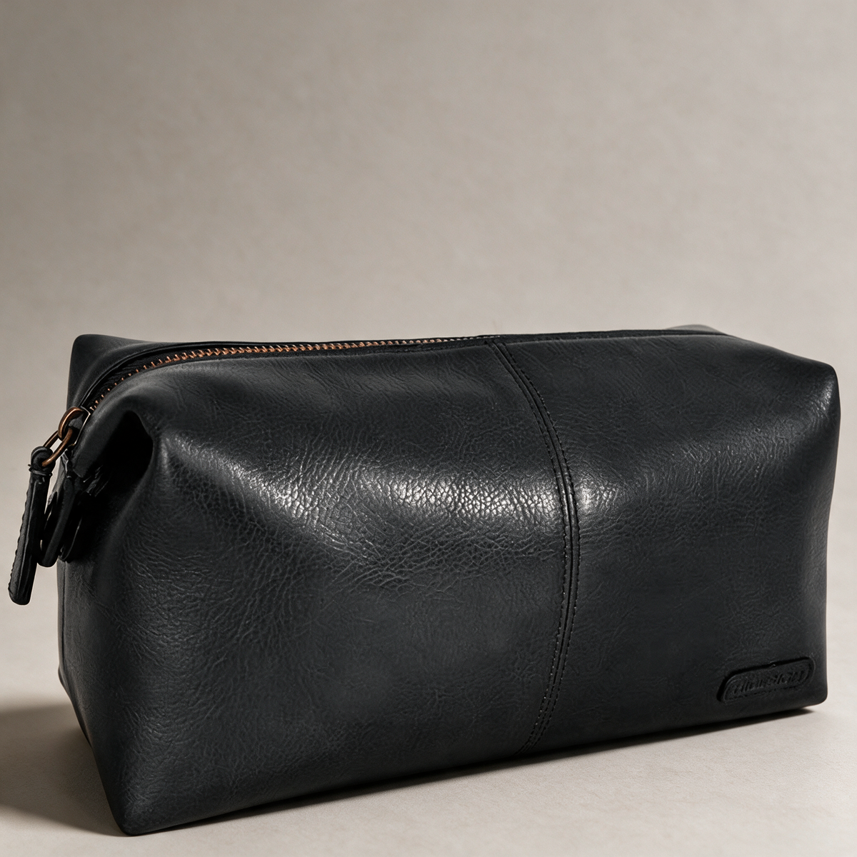 Black leather dopp kit on a warm grey studio background