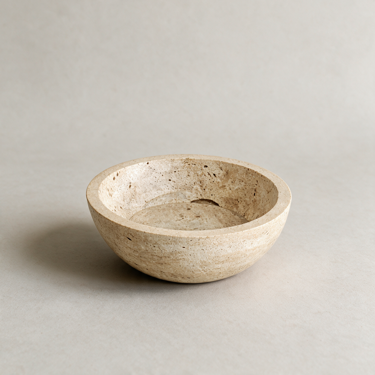 Carved travertine bowl on a warm grey studio background